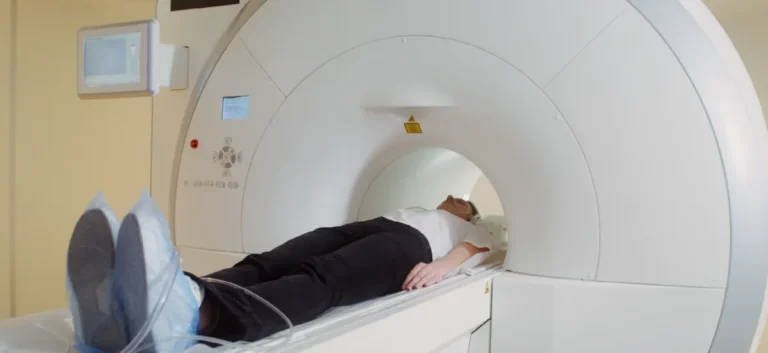 Patient wearing blue shoe covers undergoing MRI scan inside large white medical imaging machine.
