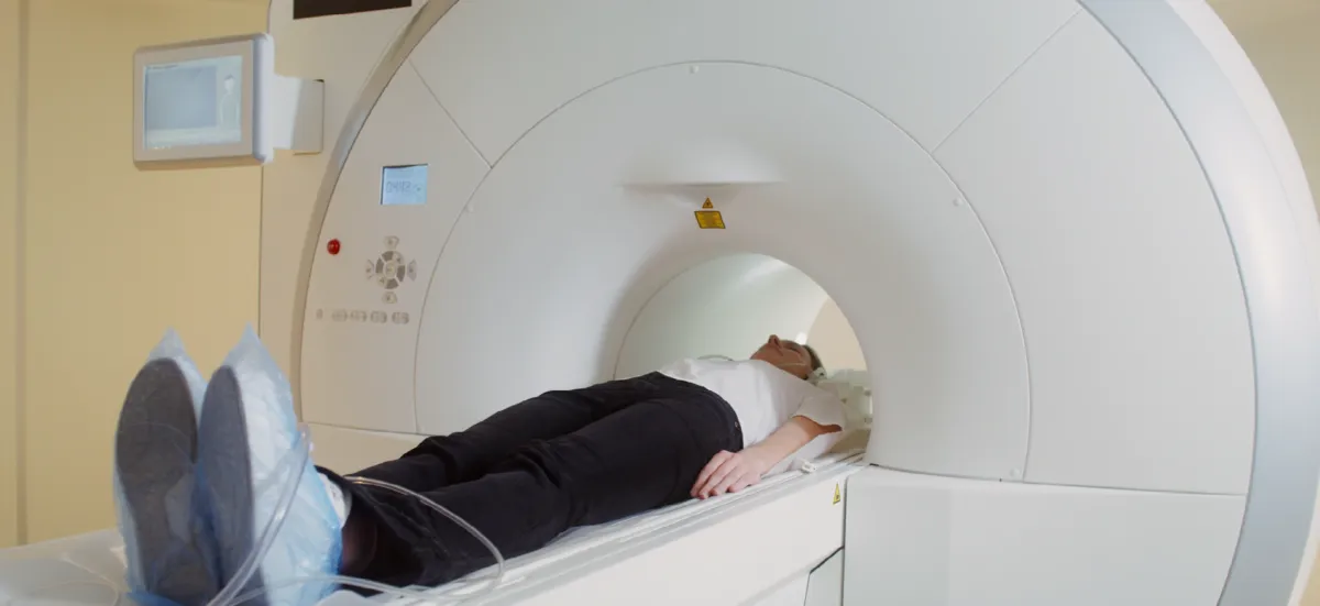 Patient wearing blue shoe covers undergoing MRI scan inside large white medical imaging machine.
