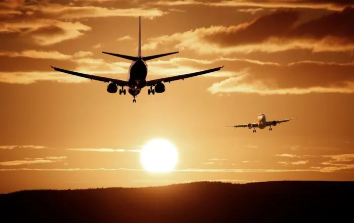 Two airplanes approaching for landing against a golden sunset sky with scattered clouds.