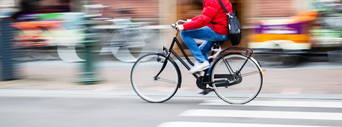 Person wearing a red jacket riding a black bicycle on a city street crosswalk.