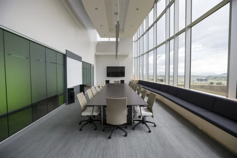Spacious modern conference room with long table, beige chairs, large windows, and city view.
