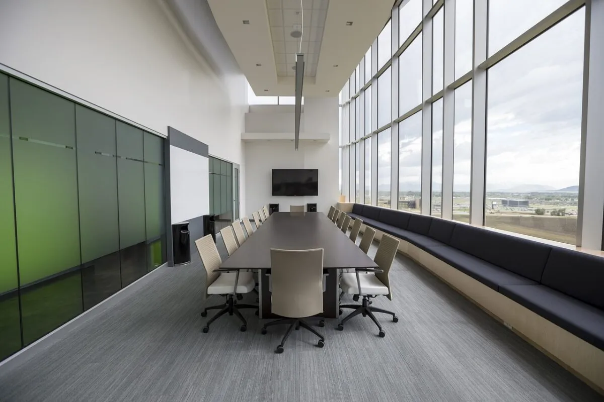 Spacious modern conference room with long table, beige chairs, large windows, and city view.