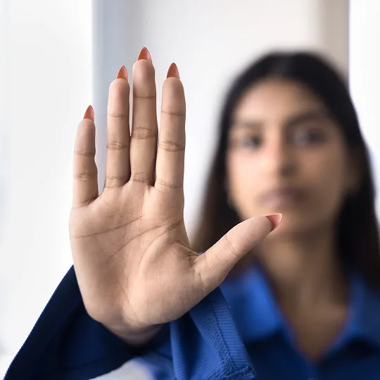 Close-up of a woman's hand raised forward with fingers spread, blurred face in background.