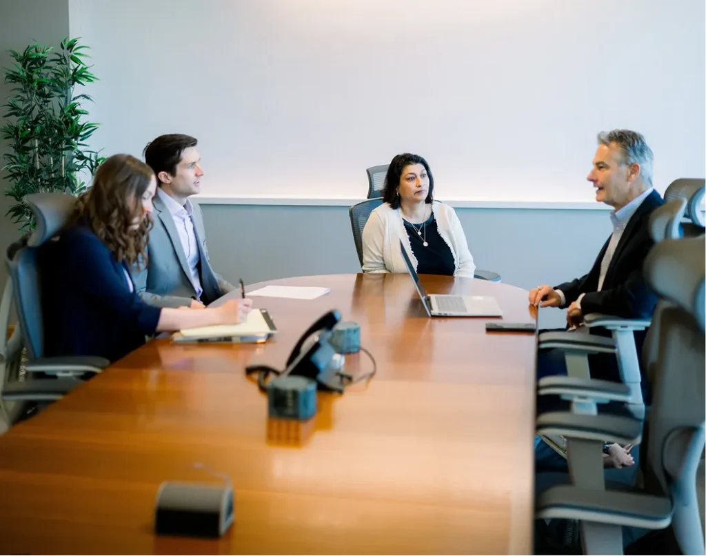 Four professionals engaged in a meeting around a wooden conference table in a modern office.
