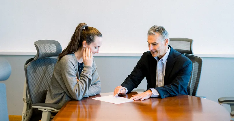 Two professionals, a woman and a man, seated at a conference table reviewing a document.