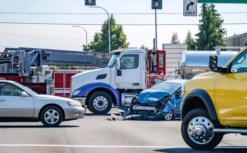Intersection scene depicting a blue car with severe front-end damage beside a white truck and fire engine.