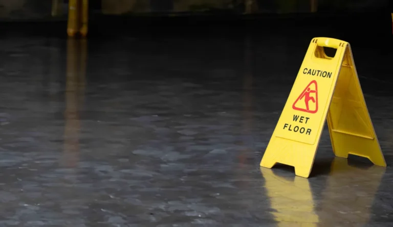 Yellow caution sign with "Caution Wet Floor" text on reflective dark floor.