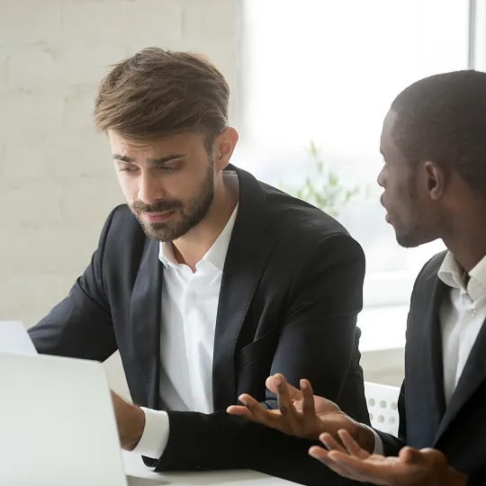 Two professional men in suits engaged in a serious discussion at a desk.