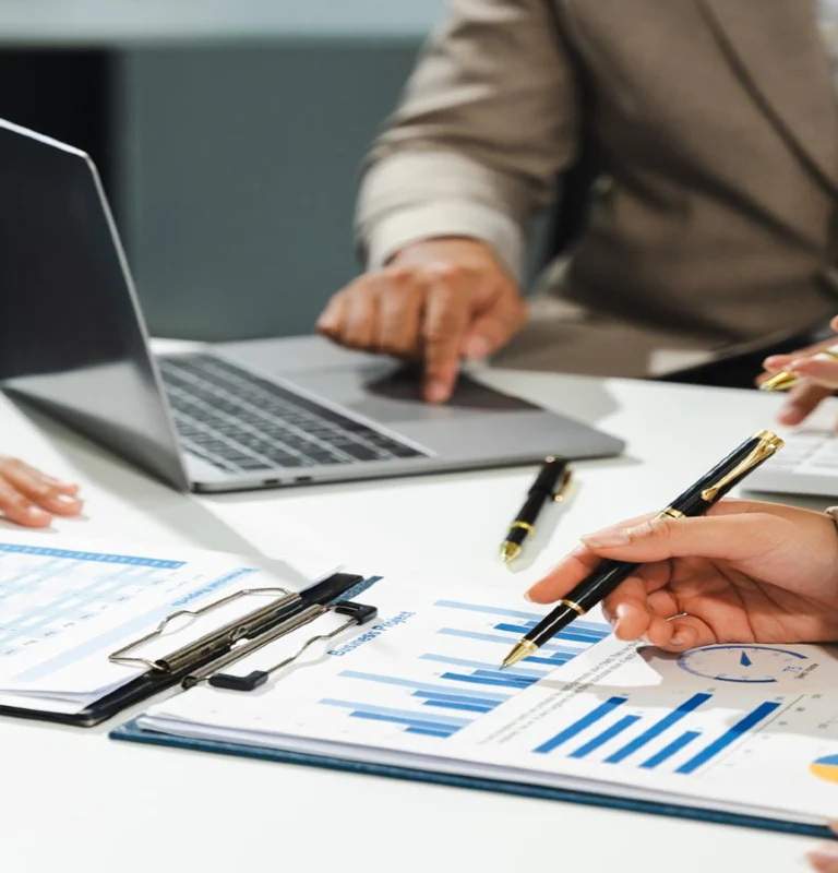 Close-up of business professionals reviewing financial charts and data with laptop and pens.