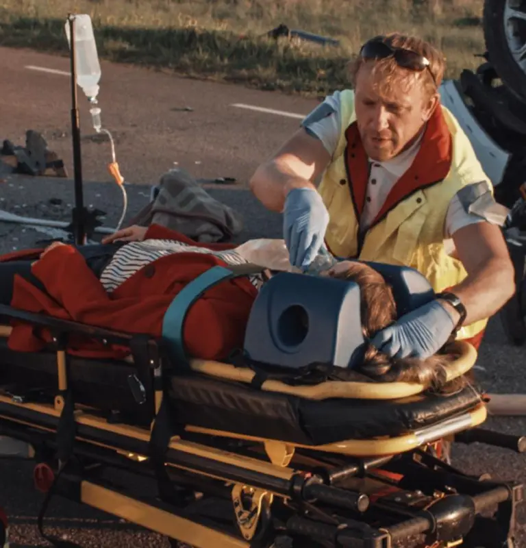 Emergency responder in yellow vest administering care to patient with neck brace on stretcher.