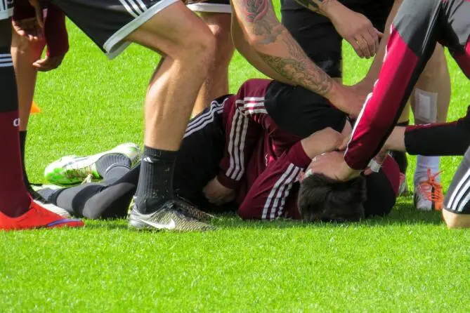 Soccer players attending to an injured teammate lying on the grass field.