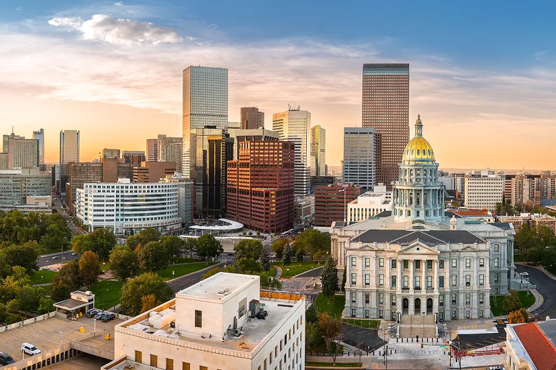 Aerial view of Denver skyline at sunset with Colorado State Capitol building and surrounding skyscrapers.