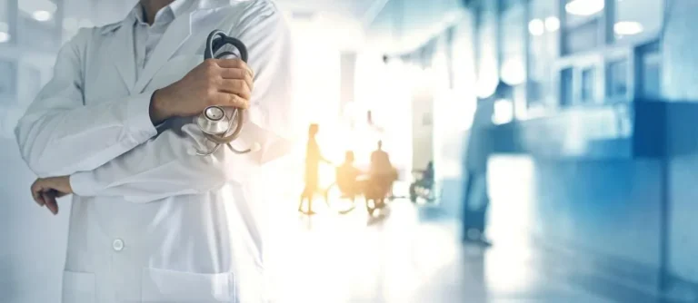 Medical professional in white coat holding stethoscope in bright hospital corridor.