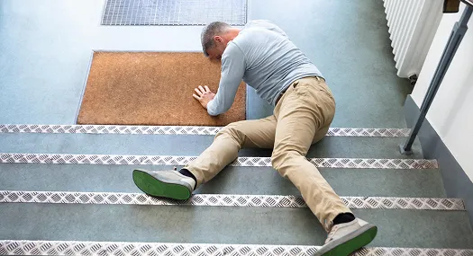 Man in gray shirt and beige pants lying on stairs after a fall.