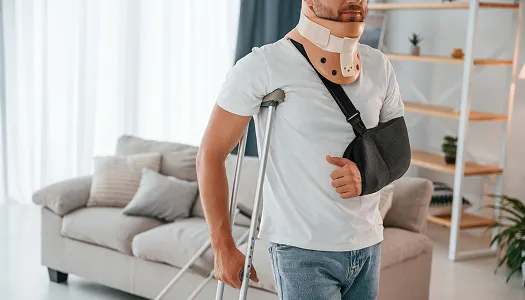 Man with neck brace, arm sling, and crutches standing in a living room.