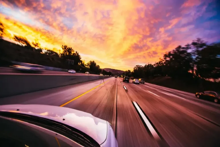 View from a moving vehicle on a highway with cars and a vibrant orange and purple sunset sky.