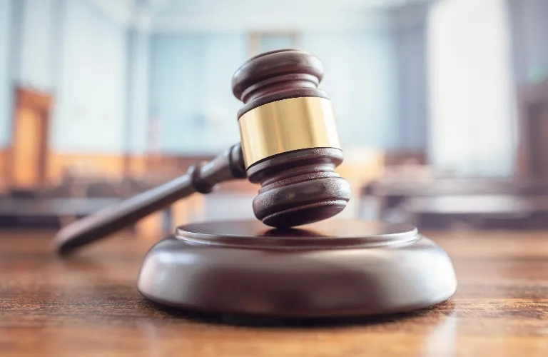 Close-up of a wooden judge’s gavel with a gold band resting on a sound block in a courtroom.