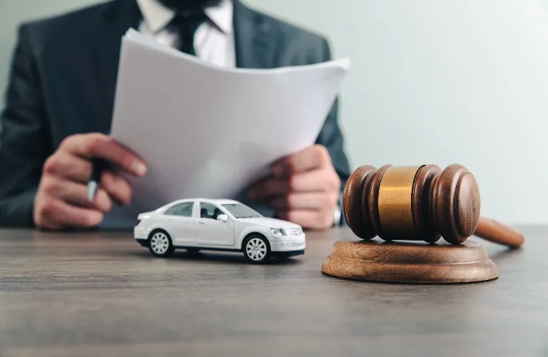 A wooden judge's gavel, a white toy car, and a person in a suit holding documents.