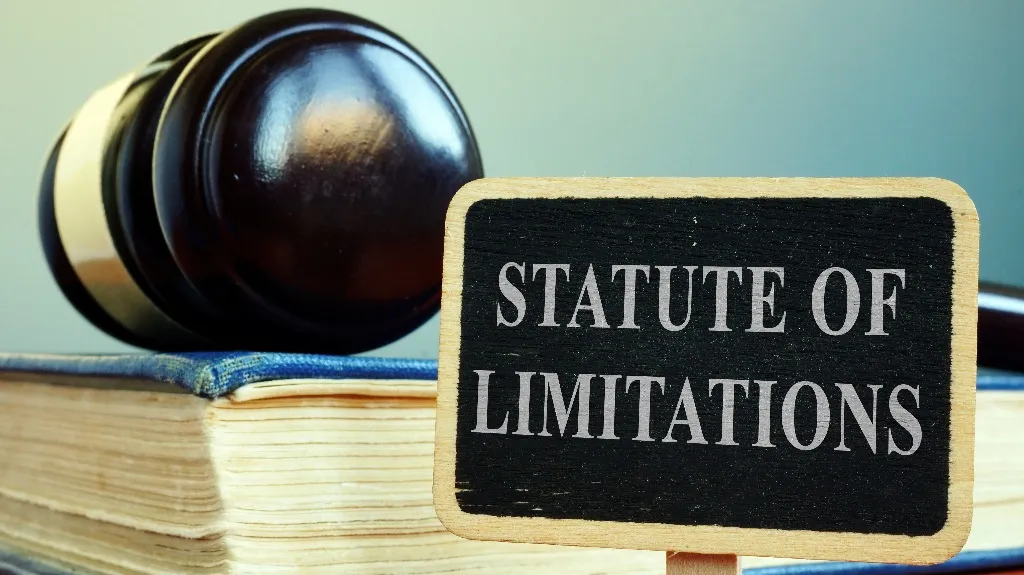 Wooden judge's gavel resting on a book next to a small sign reading "Statute of Limitations.