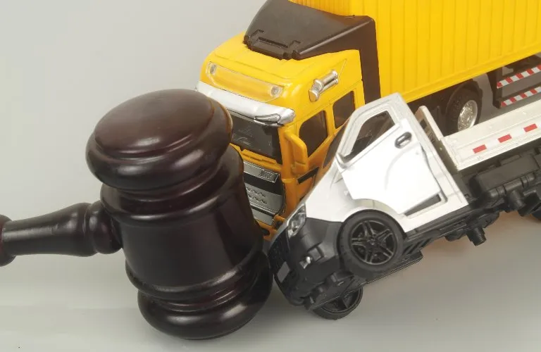 Dark wooden judge's gavel next to yellow and white toy trucks on a gray surface.
