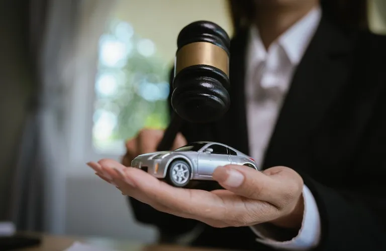 Person in formal attire holding a toy silver car under a judge's gavel.