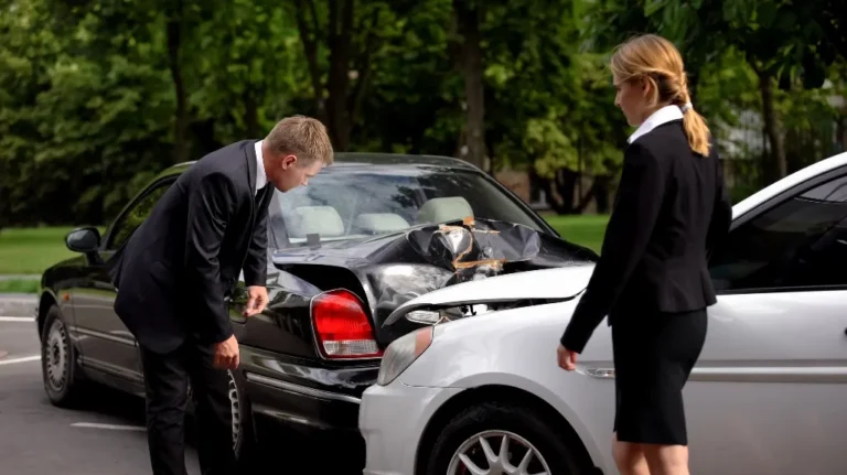 Two professionally dressed individuals inspecting damage after a car collision in a parking lot.