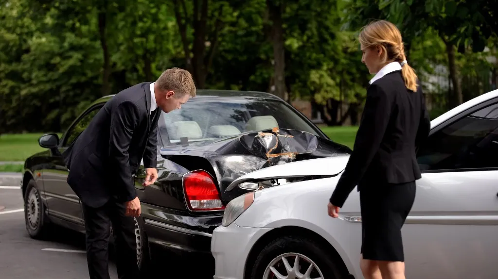 Two professionally dressed individuals inspecting damage after a car collision in a parking lot.