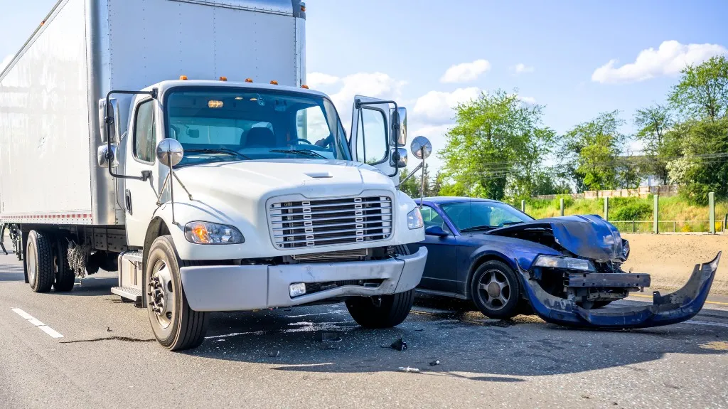 White box truck and blue sedan involved in a collision on a sunny highway.