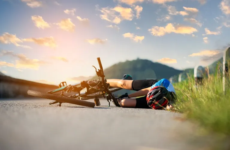 Cyclist wearing helmet lying on road next to fallen bicycle during sunset.
